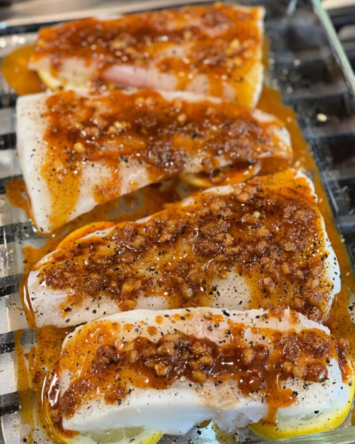 A seasoned oil sauce drizzled over cod filet in a glass baking dish.