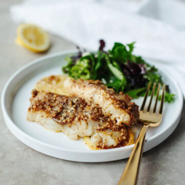 Cajun baked cod served on a white plate with a salad.