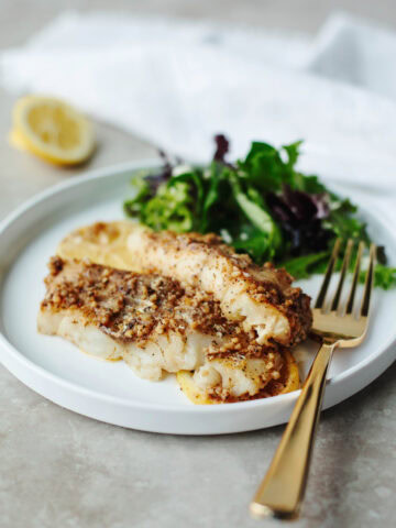 Cajun baked cod served on a white plate with a salad.
