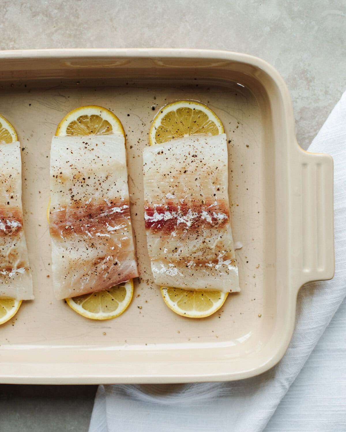 Unbaked fish filet placed over lemon slices in a baking pan.