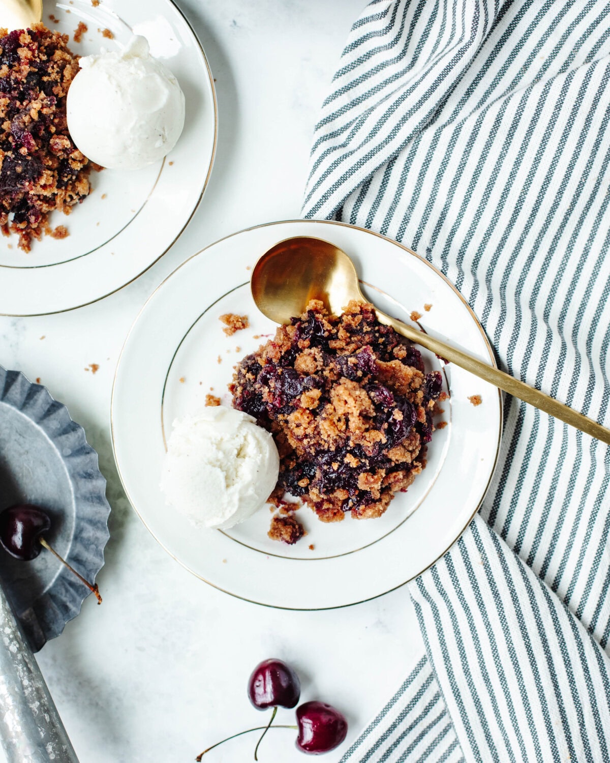 A serving of cherry cobbler on a white plate with ice-cream and a gold spoon.