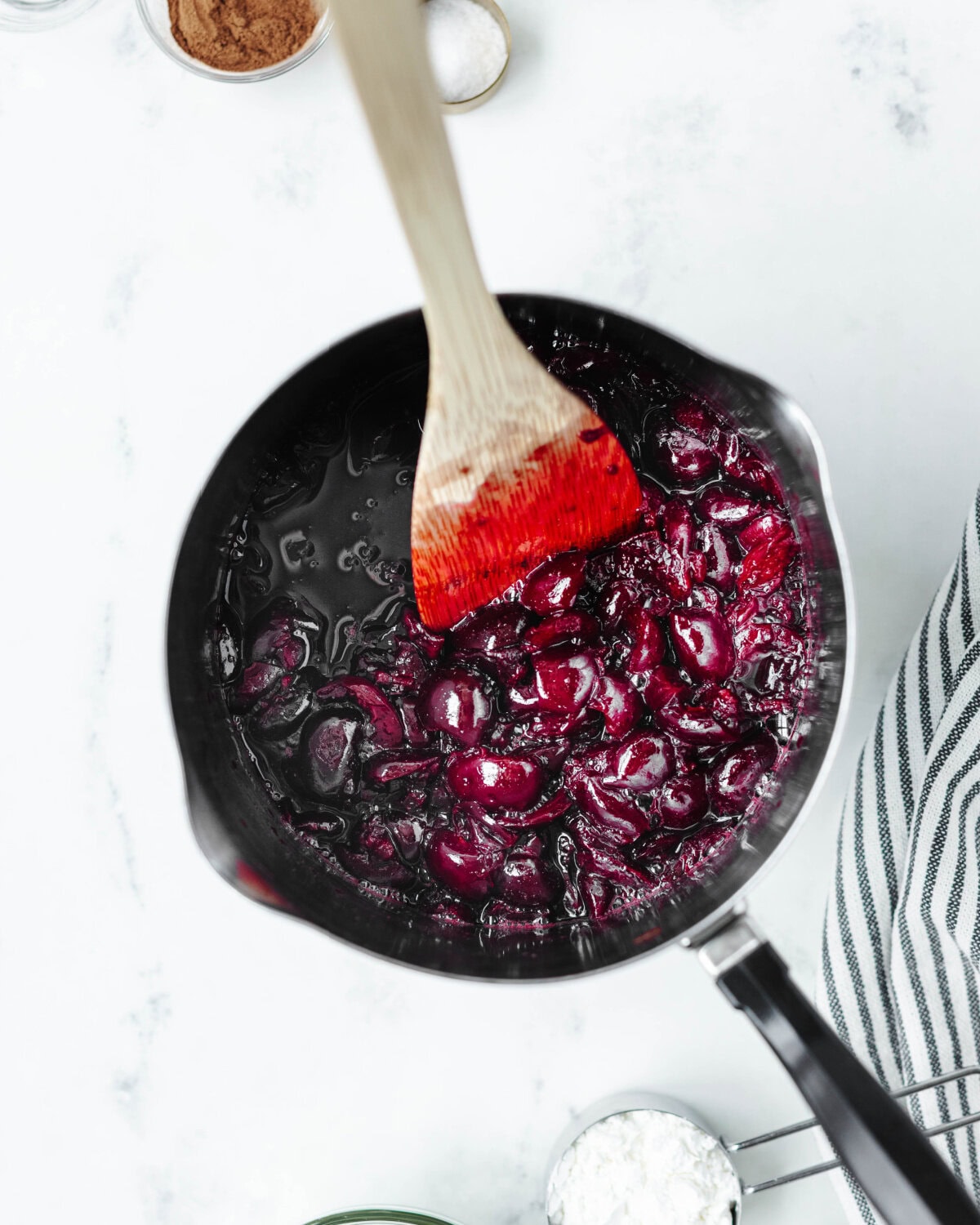Cherries simmering in a saucepan until softened.