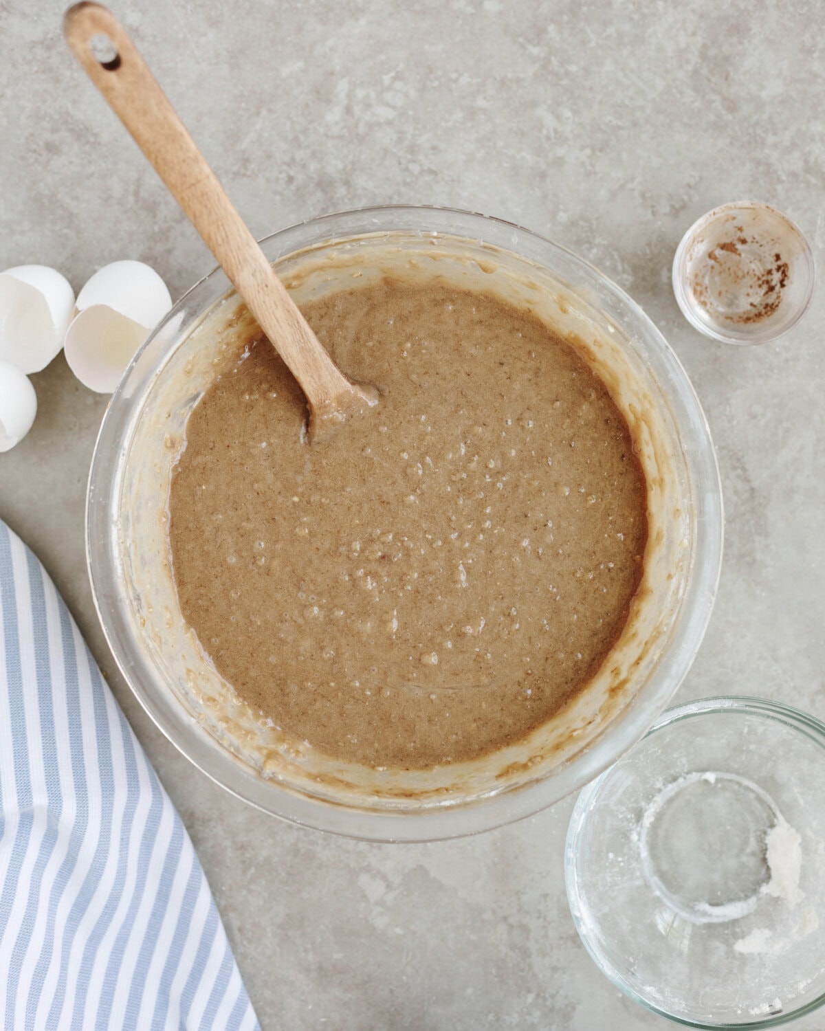 Cake batter mixed together in a glass mixing bowl using a wood spoon.