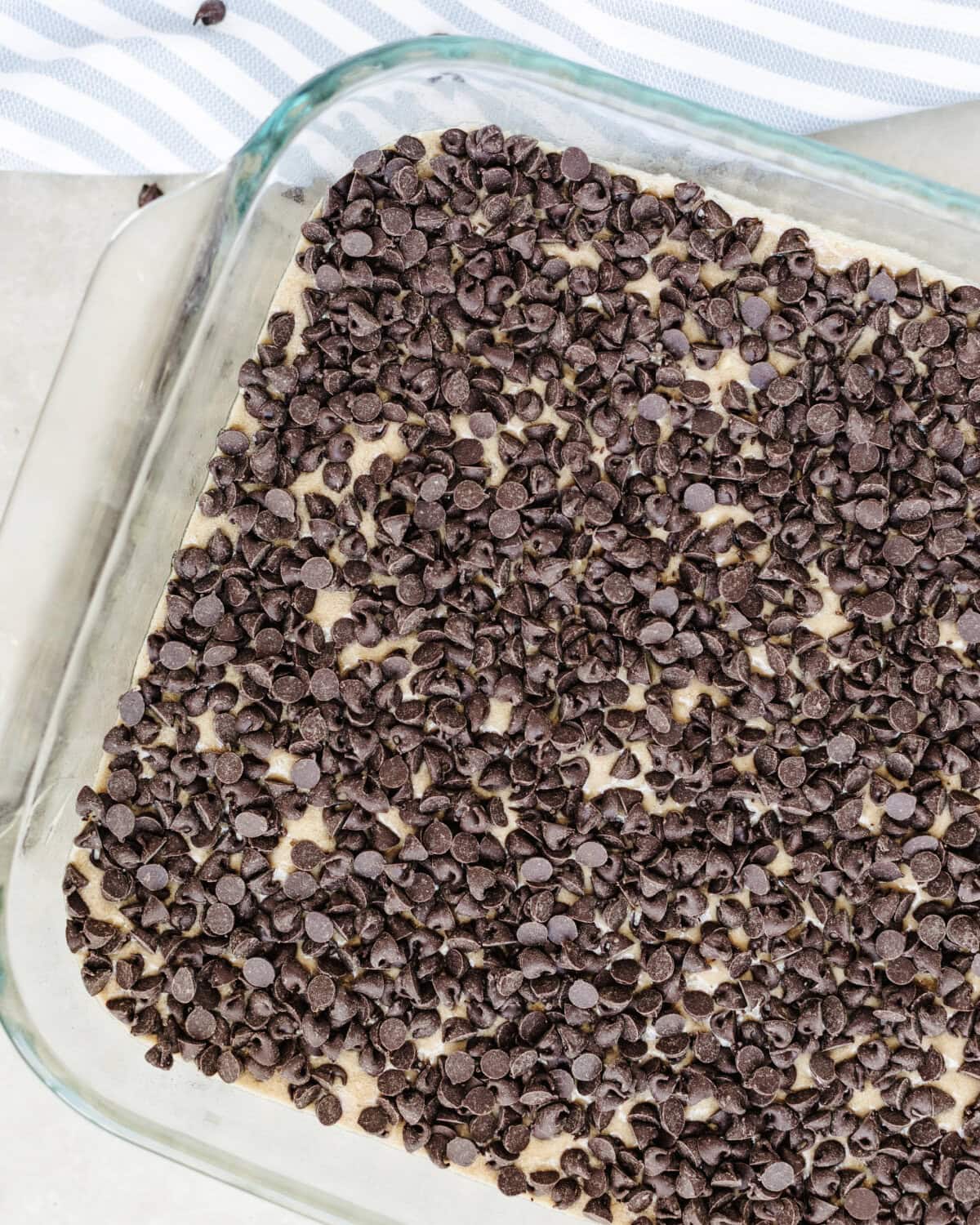 Mini chocolate chips sprinkled on top of chocolate cake batter in a glass 9x13 baking pan.