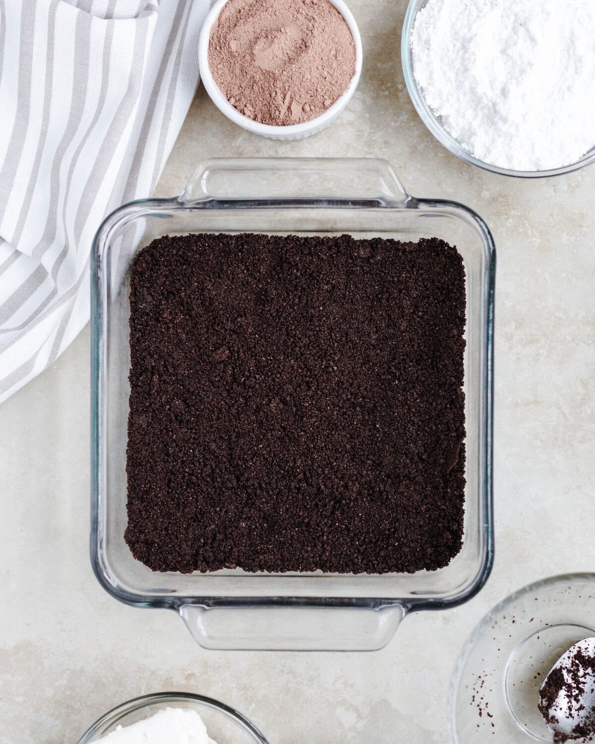 Oreo crumbs pressed into the bottom of a glass 8x8 baking pan.