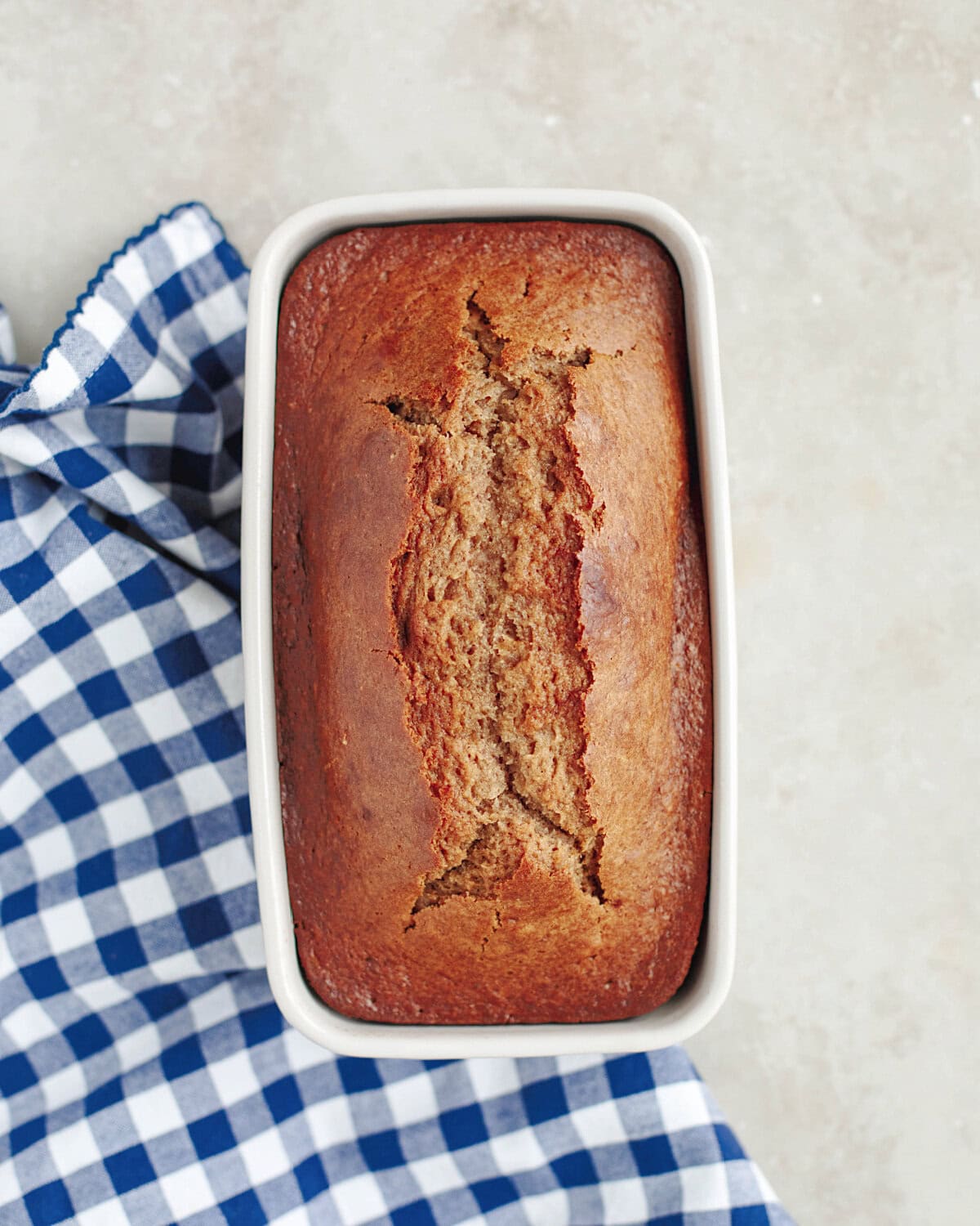 A baked loaf of cinnamon applesauce bread in a white loaf pan.