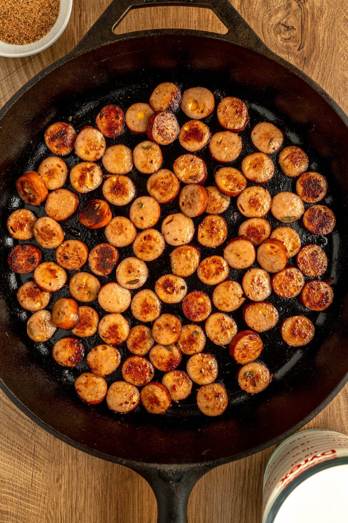 Sliced smoked sausage browning in a cast iron skillet.