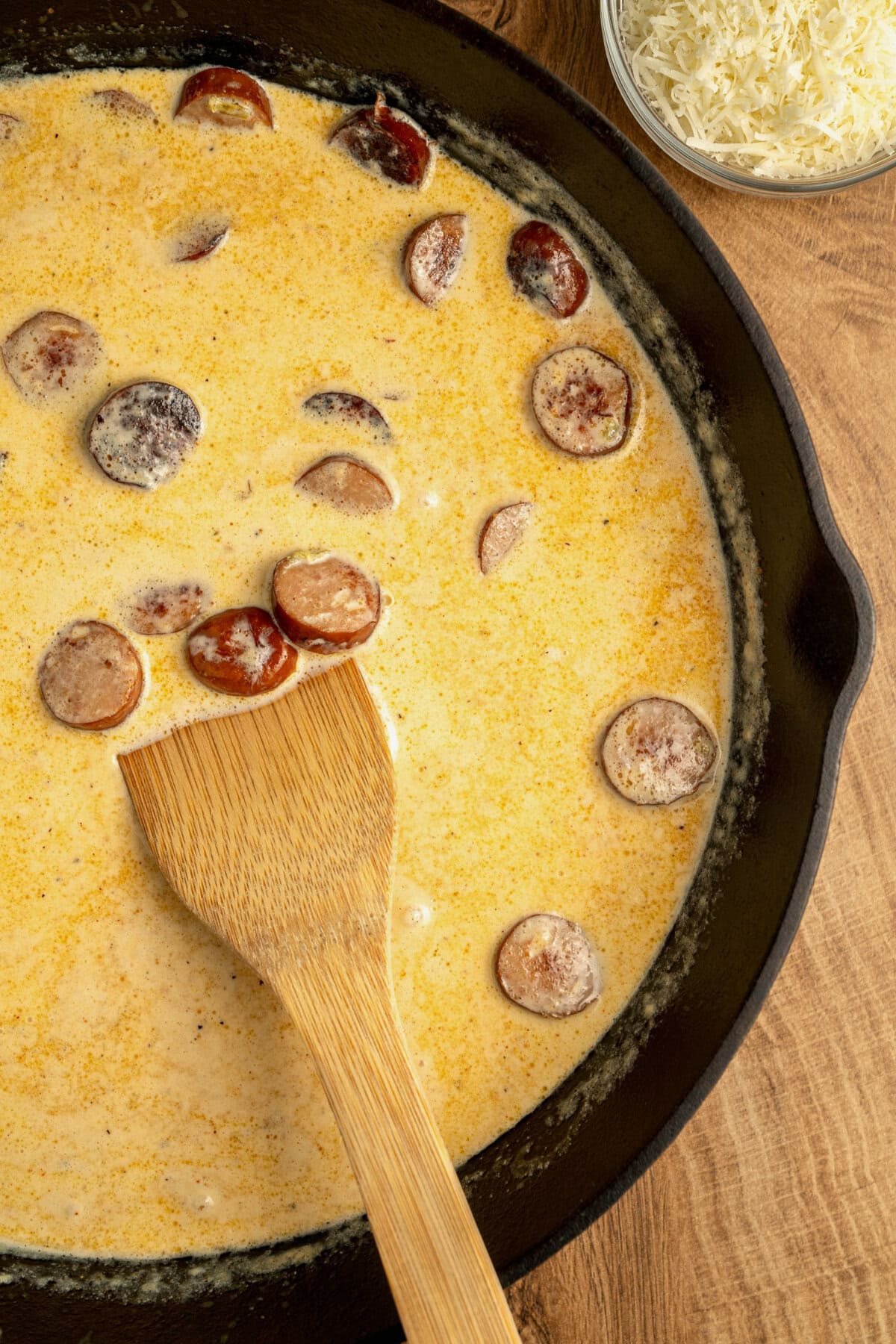 Heavy cream, smoked sausage, and Cajun seasoning simmering in a skillet.