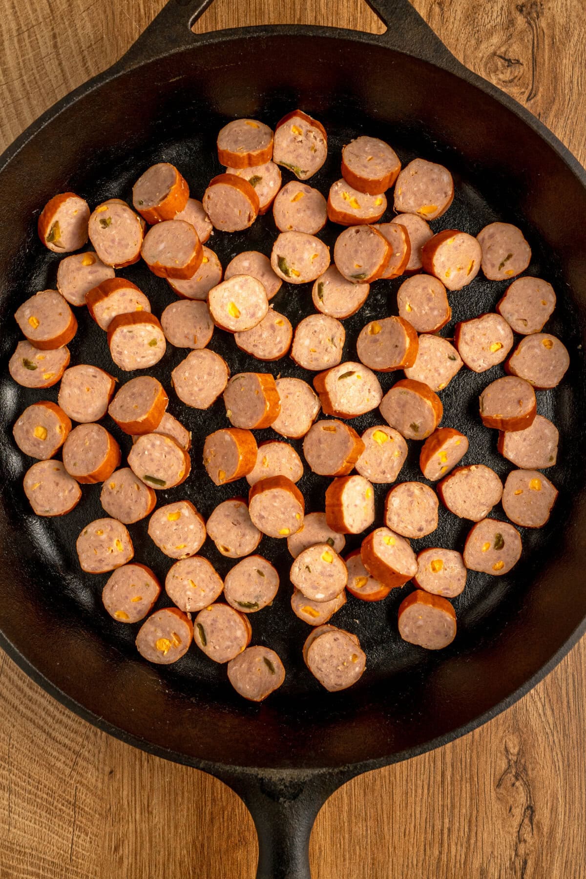 Sliced sausage added to a cast iron skillet.