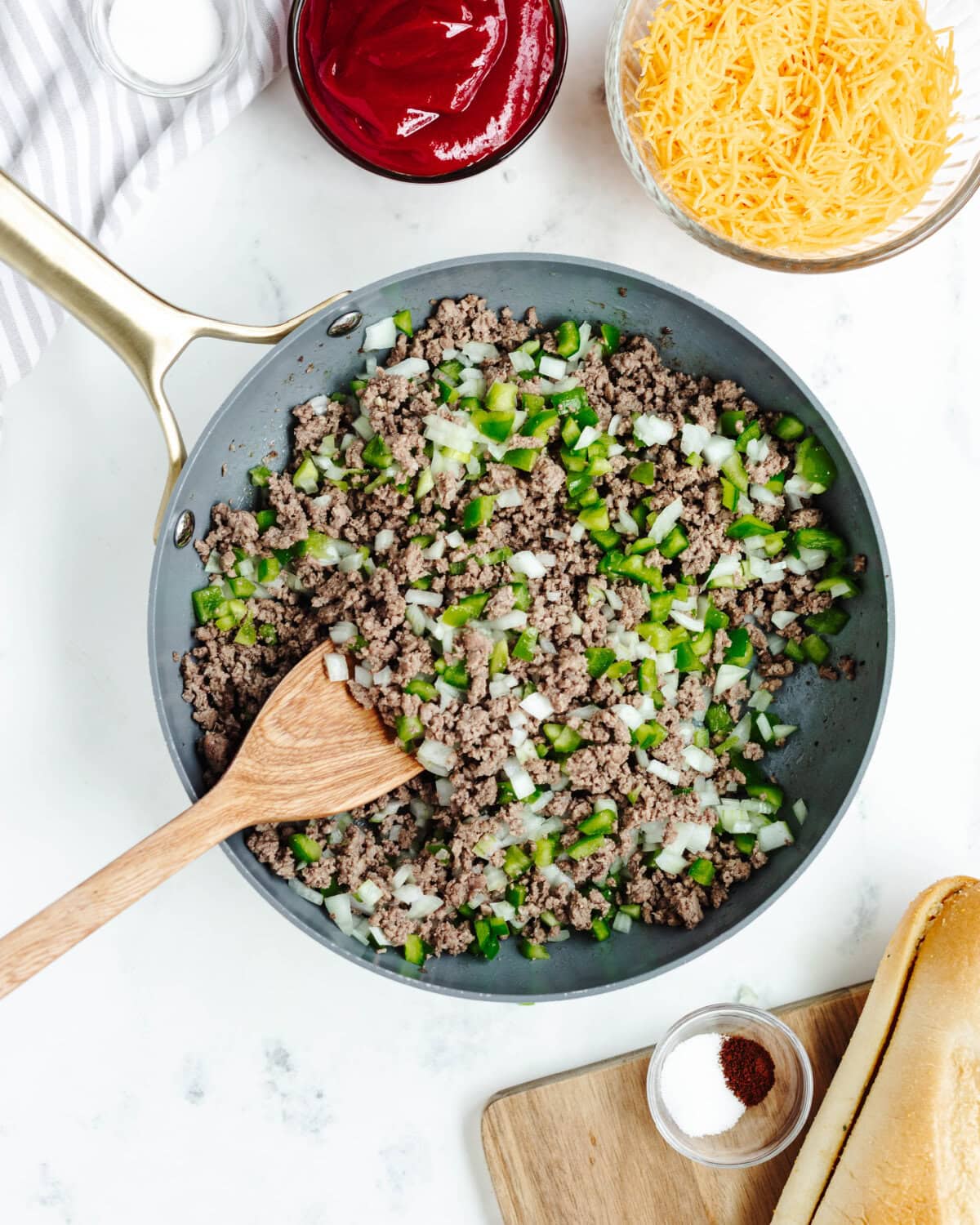 Diced green bell peppers and onions cooking with ground beef in a skillet.