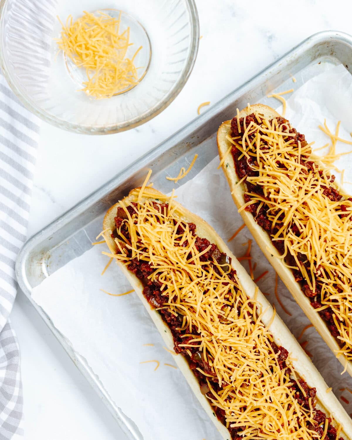 Shredded cheese sprinkled on top of a ground beef mixture on top of garlic bread.