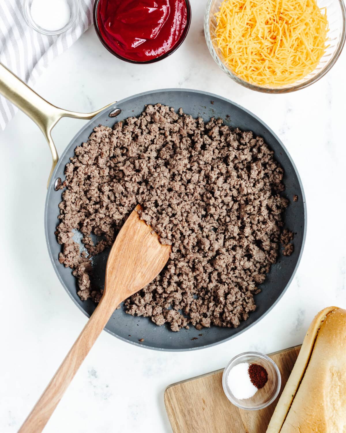 Ground beef cooking in a skillet with a wood spoon.