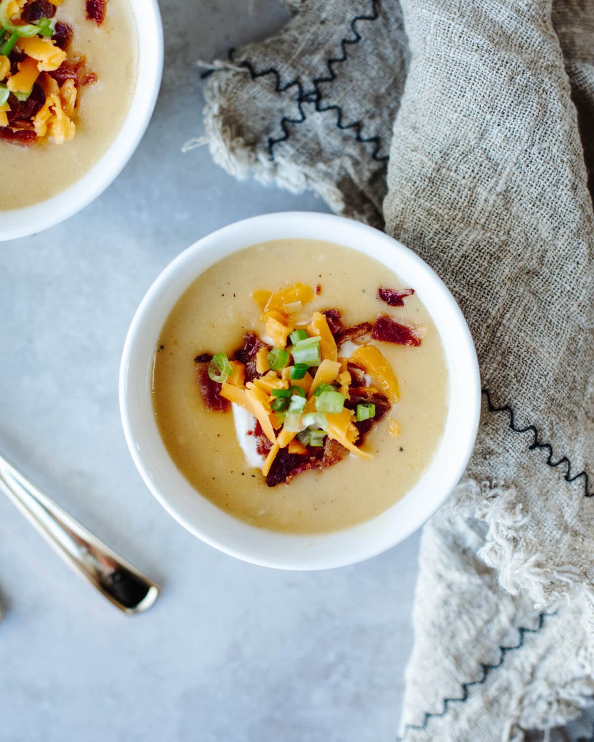An overhead look at a white bowl of potato soup topped with bacon, cheese, green onions, and sour cream.