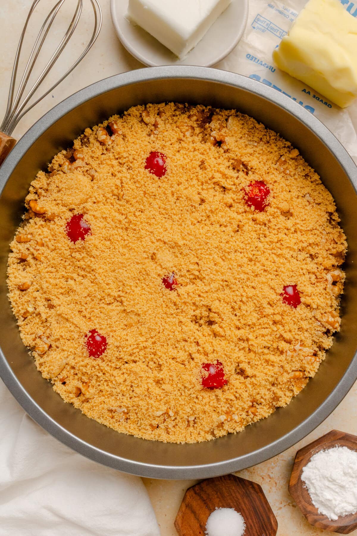 Brown sugar sprinkled over walnuts and maraschino cherries in a round cake pan.
