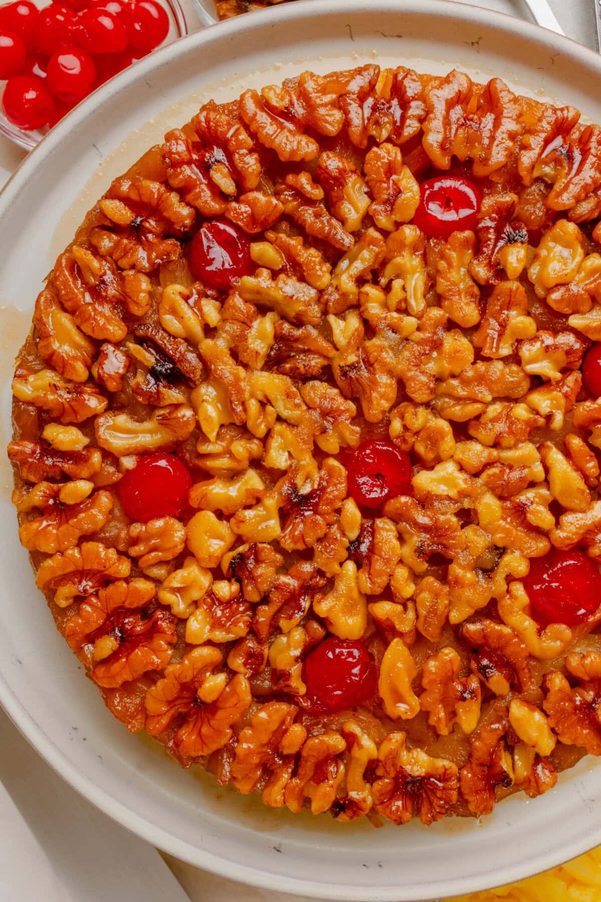 Overhead view of homemade cake topped with crushed pineapple, walnuts, and maraschino cherries.