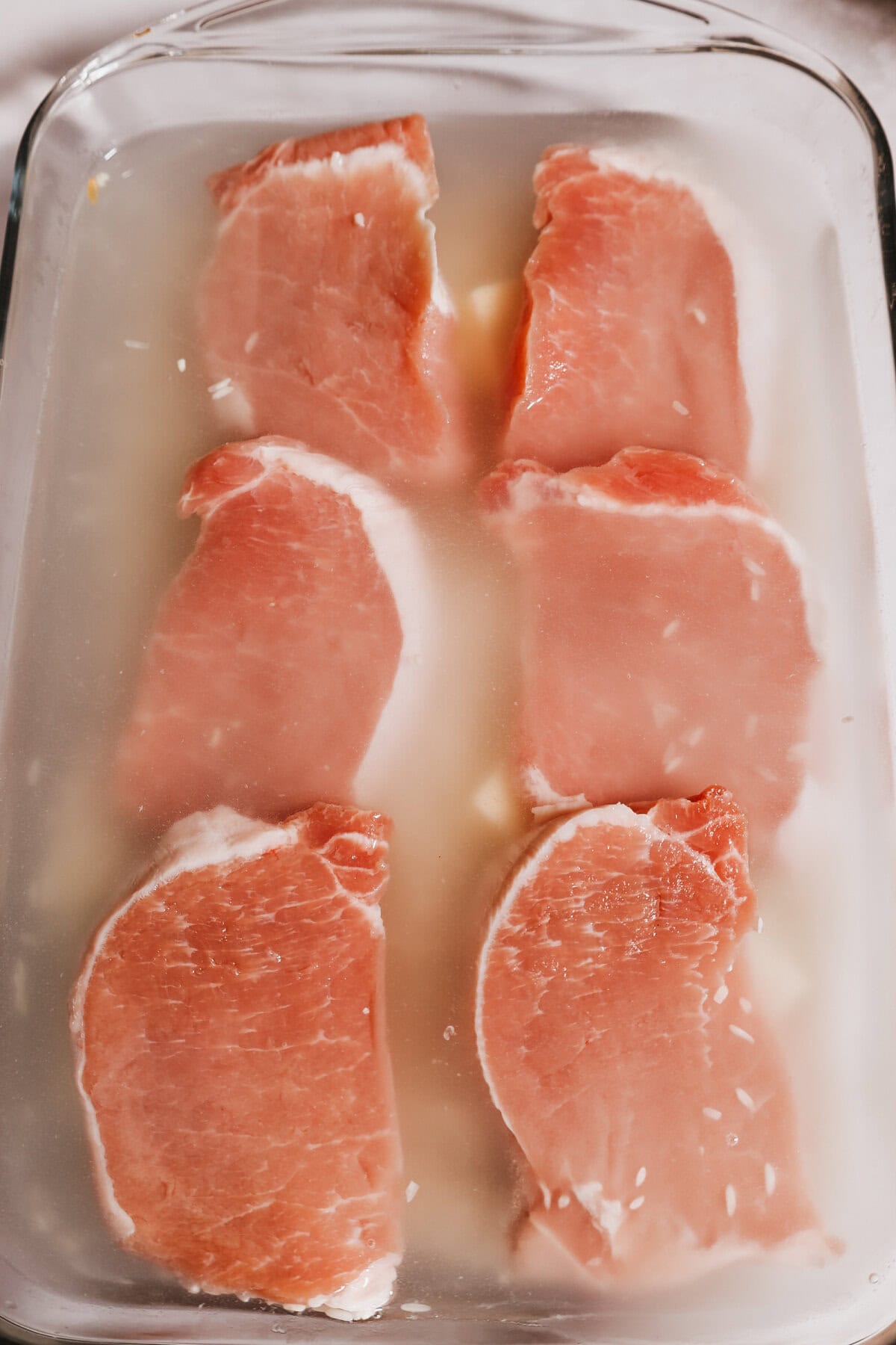 Pork chops lined in a glass baking dish with water and rice.
