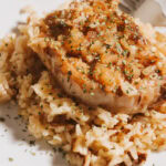 A cooked pork chop with rice on a white plate.