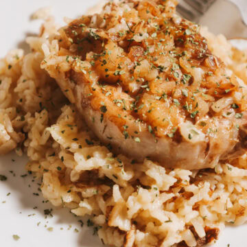 A cooked pork chop with rice on a white plate.