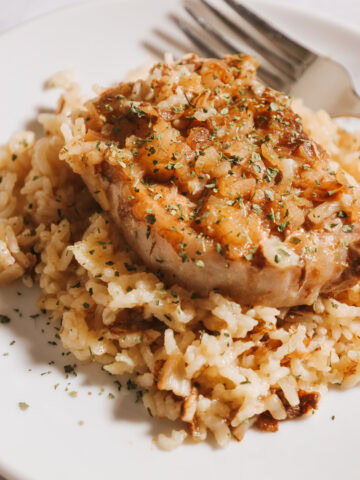 A cooked pork chop with rice on a white plate.
