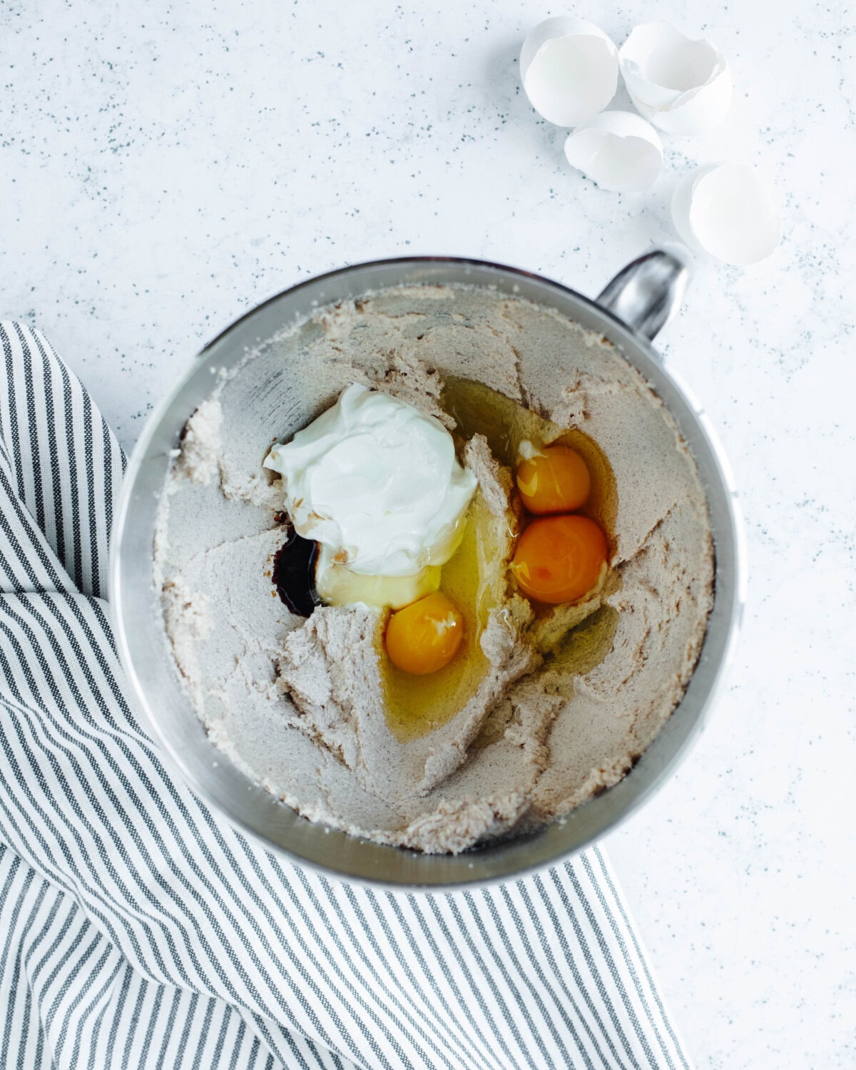 Eggs, vanilla, and sour cream added to a creamed butter mixture in a mixing bowl.