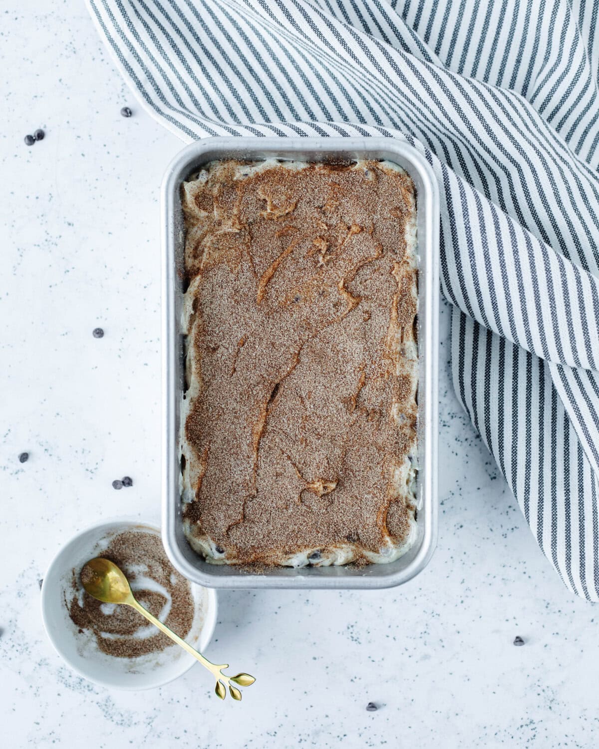 Cinnamon and sugar sprinkled on top of quick bread batter in a loaf pan.