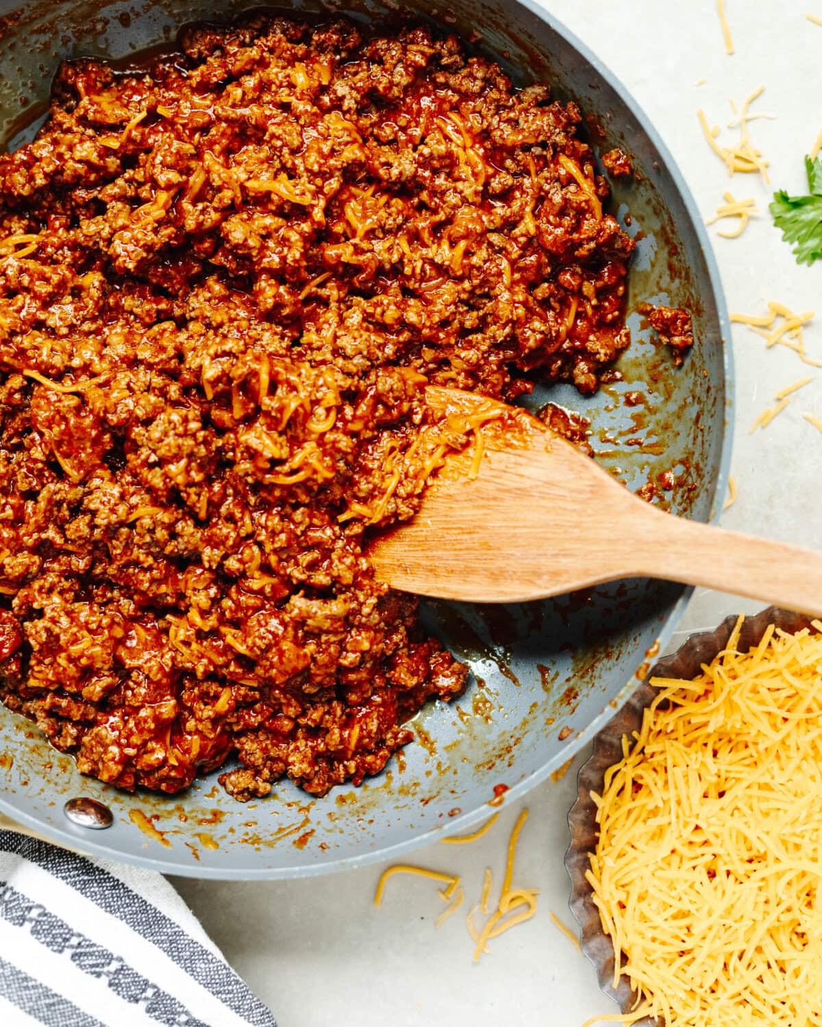 Shredded cheese added into a ground beef mixture in a skillet.