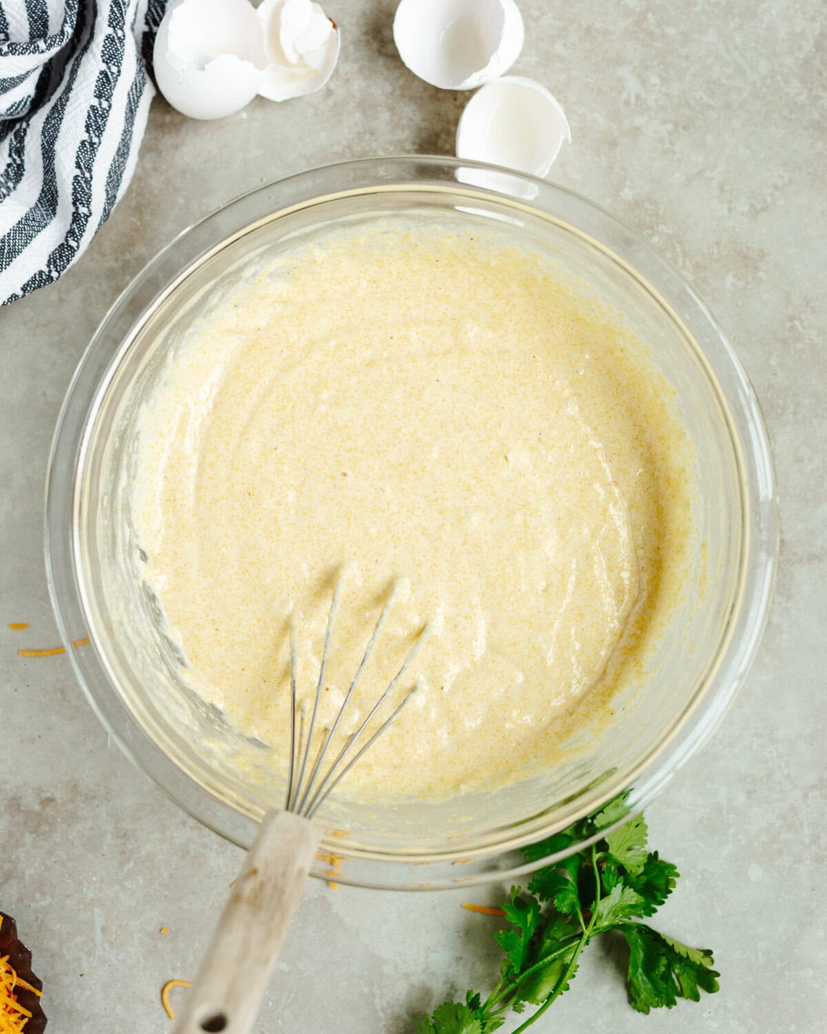Cornbread mix combined in a glass mixing bowl using a wooden spoon.