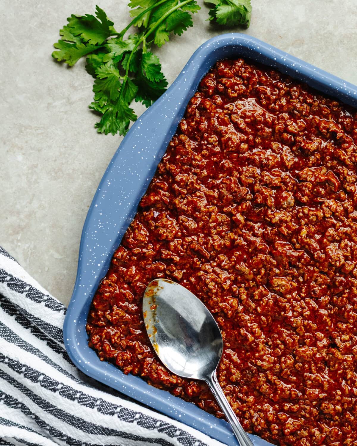 Seasoned ground beef combined with chili and cheese and spread evenly into a prepared cookie sheet.