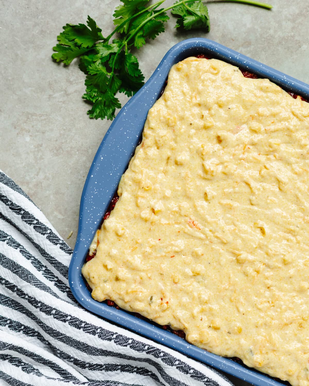Jiffy cornbread mix spread on top of a taco seasoned beef mixture in a cookie sheet pan.