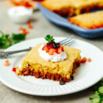 A slice of taco cornbread casserole on a white plate with toppings.