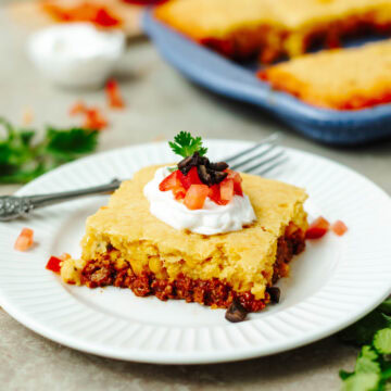 A slice of taco cornbread casserole on a white plate with toppings.