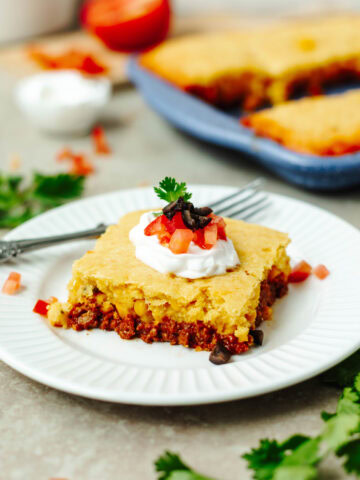 A slice of taco cornbread casserole on a white plate with toppings.