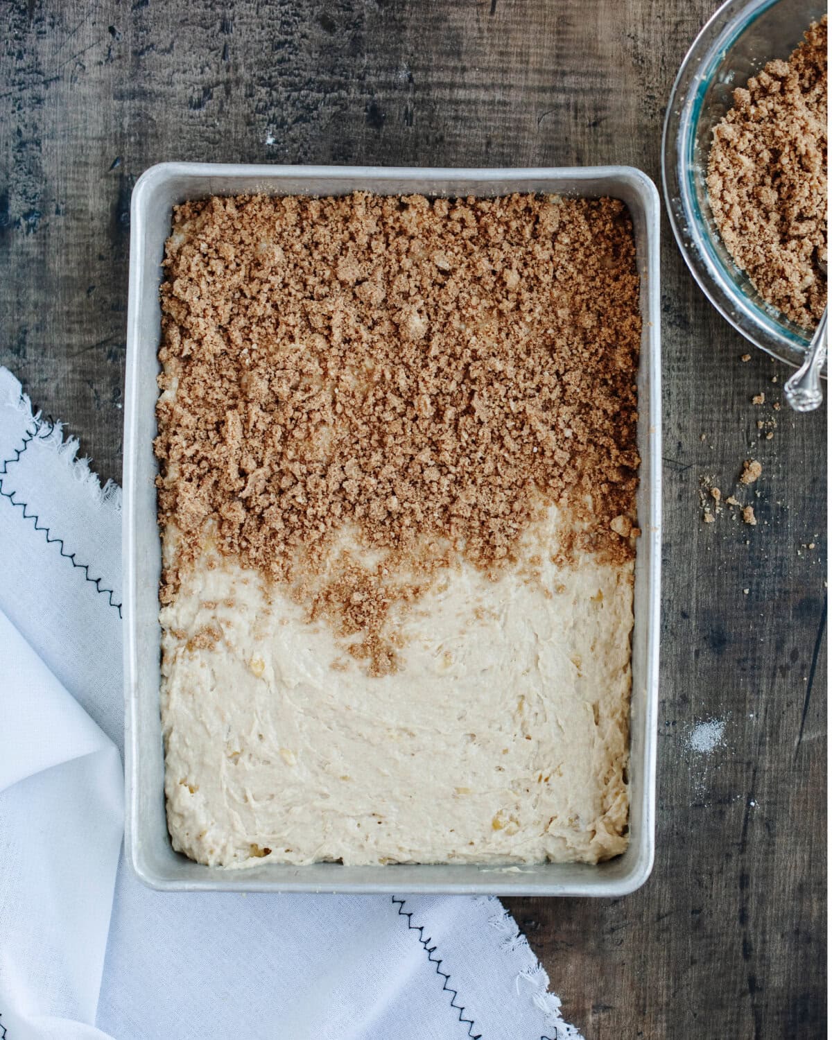 Cinnamon streusel sprinkled on top of coffee cake batter in a 9x13 baking pan.