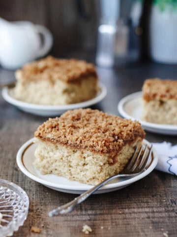 A slice of banana coffee cake on a small white plate with a fork.