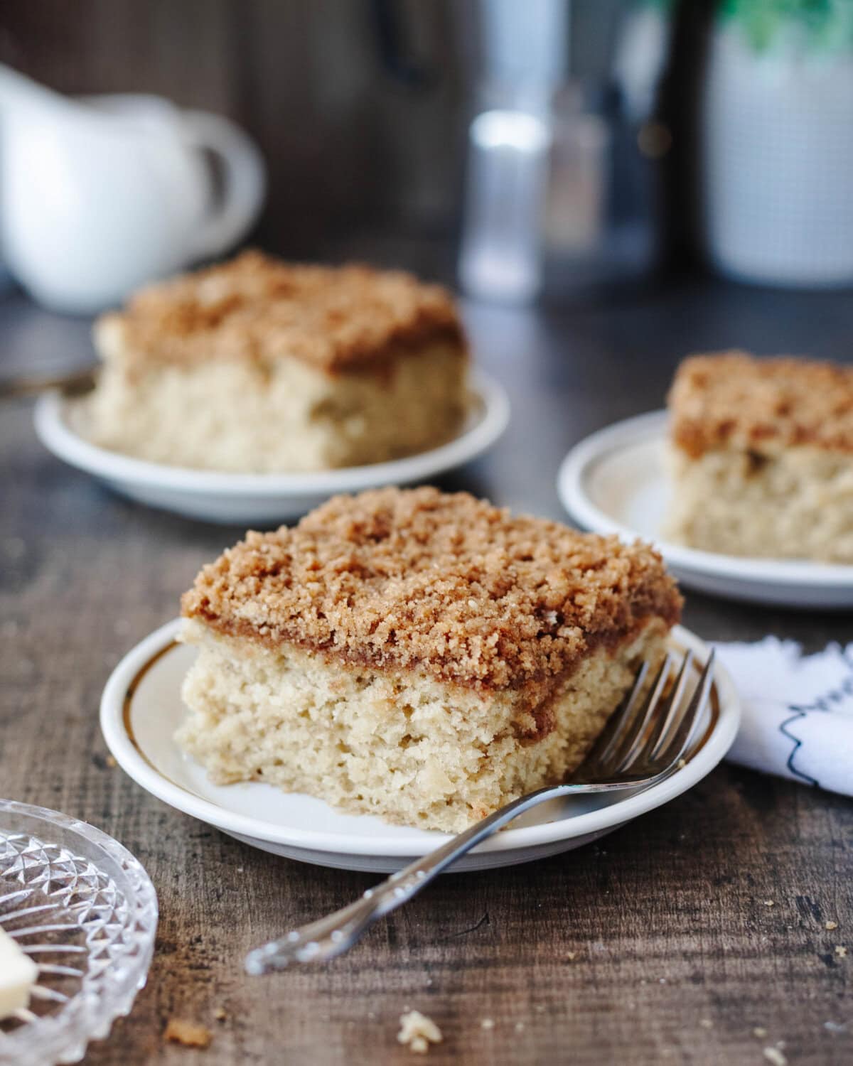 A slice of banana coffee cake on a small white plate with a fork.