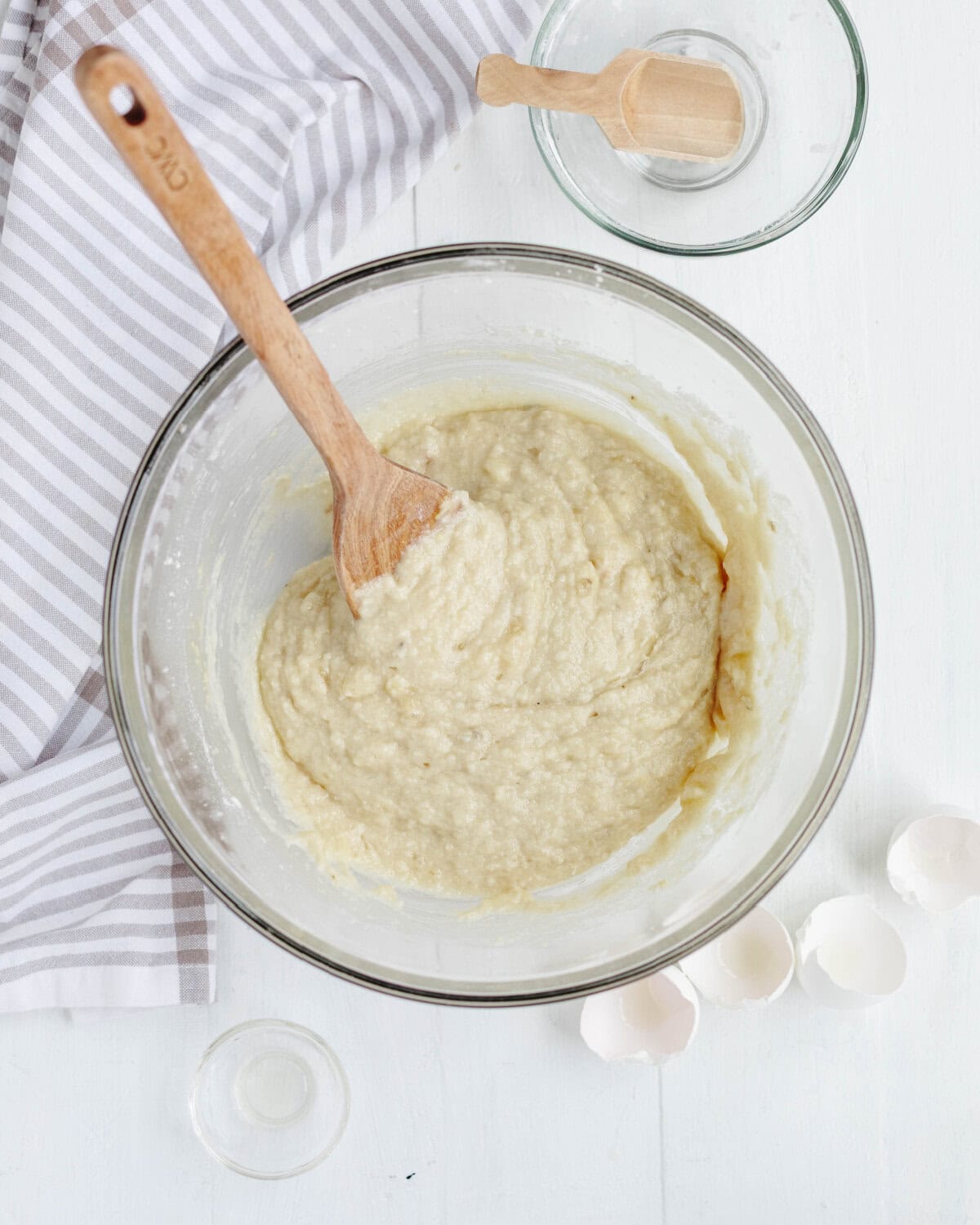 Eggs, mashed banana, and bourbon folded into dry ingredients in a glass mixing bowl.