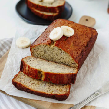 A loaf of baked bourbon banana bread sliced on a wood cutting board.
