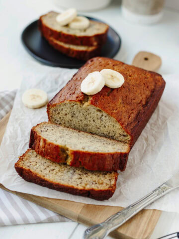 A loaf of baked bourbon banana bread sliced on a wood cutting board.