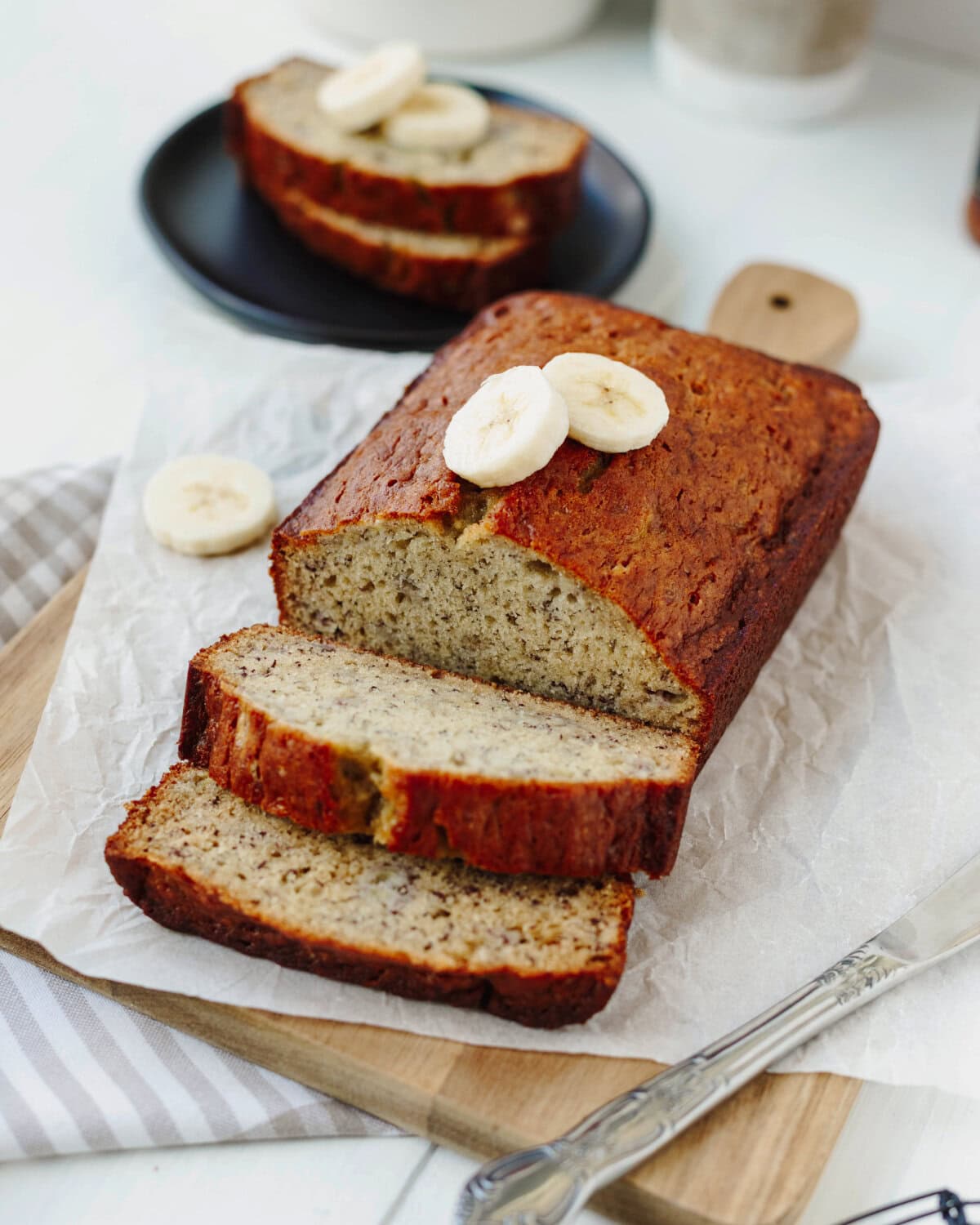 A loaf of baked bourbon banana bread sliced on a wood cutting board.