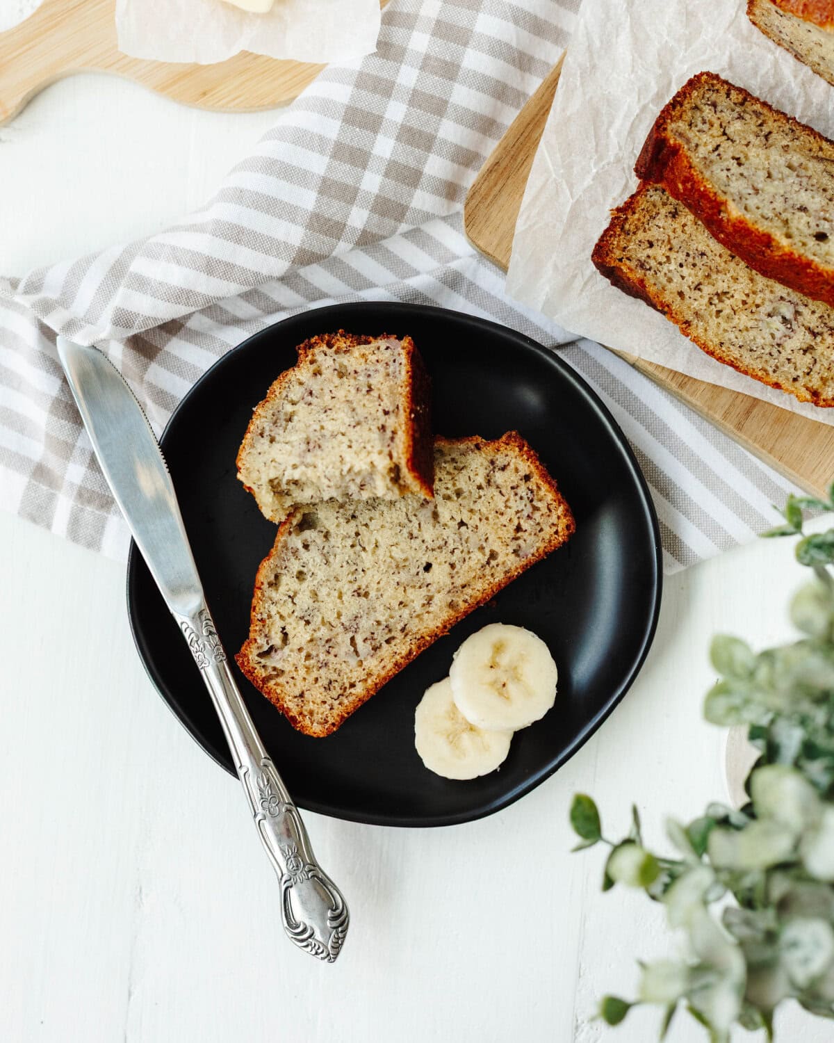 Sliced Bourbon banana bread on a black plate with some butter.