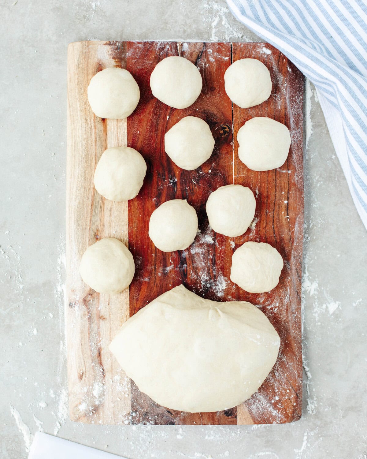 Fresh dough broken into smaller pieces and rolled into balls on a floured wood cutting board.