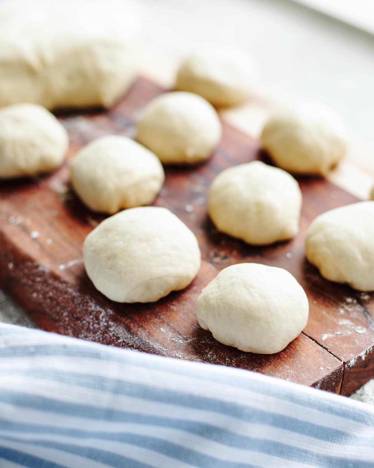 Dough balls rolls into balls on a wood cutting board.