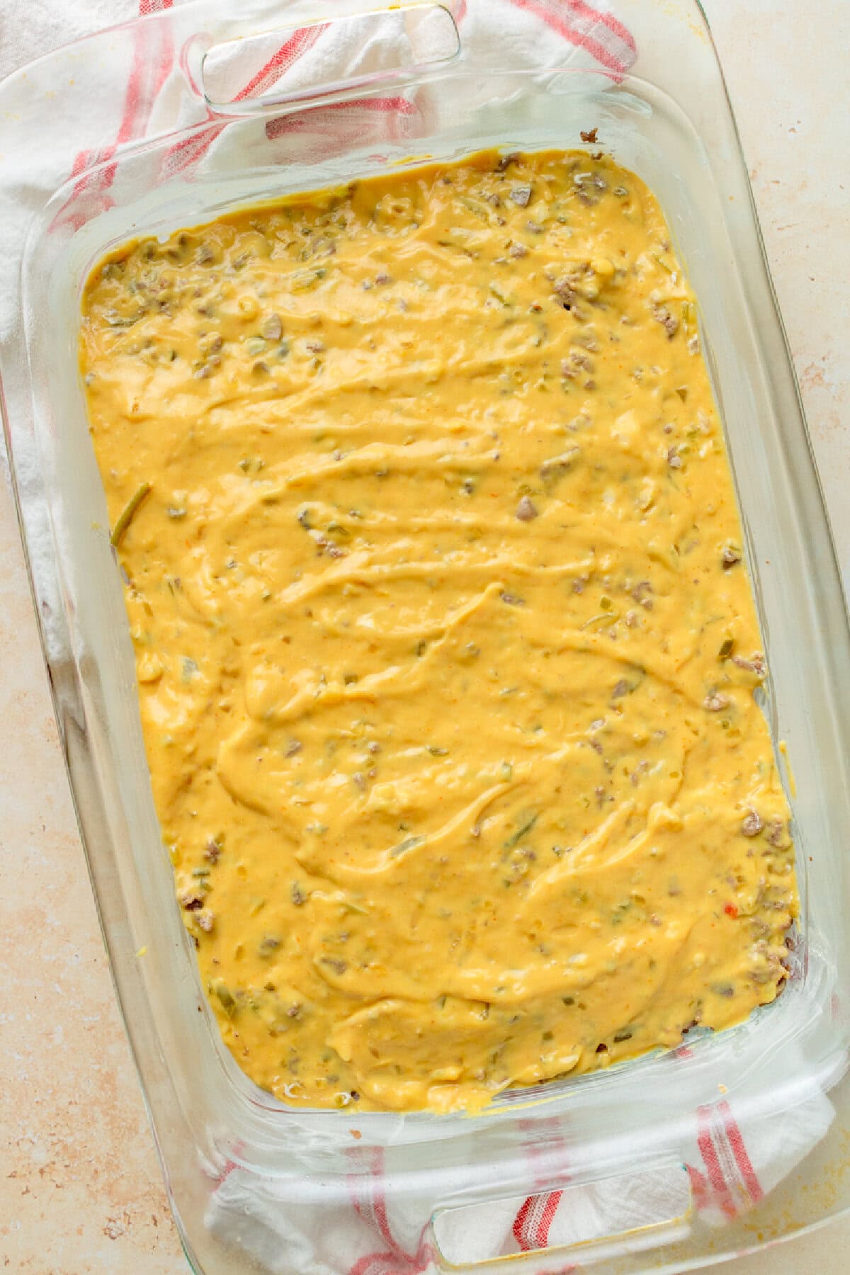 A creamy mushroom soup, mustard, ketchup mixture spread evenly over seasoned cooked ground beef in a baking dish.