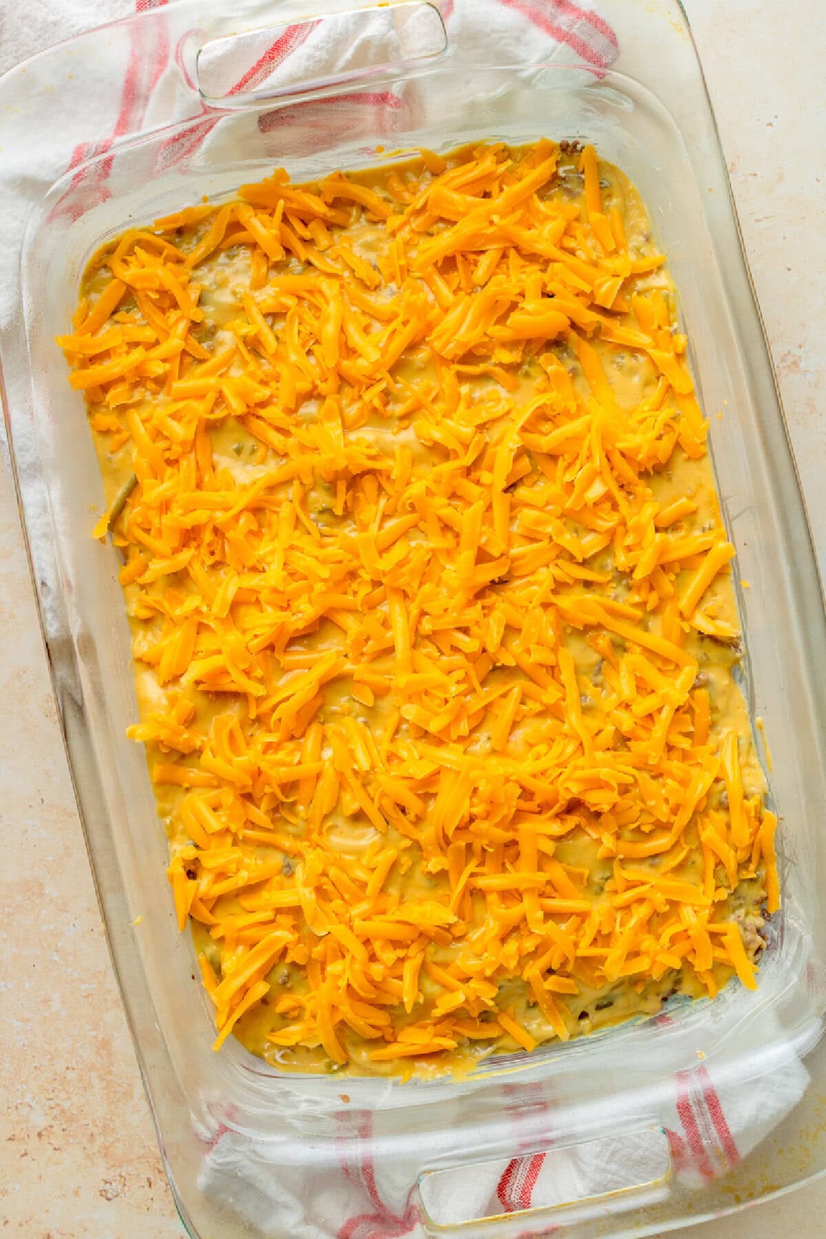 Shredded Cheddar cheese sprinkled on top of a ground beef mixture in a 9x13 baking dish.