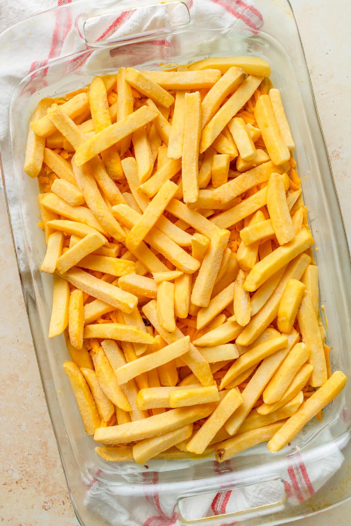 Frozen French fries sprinkled on top of a ground beef mixture in a baking dish.