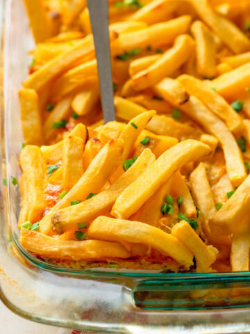 A spatula serving Cheeseburger French Fry Casserole from a glass baking pan.