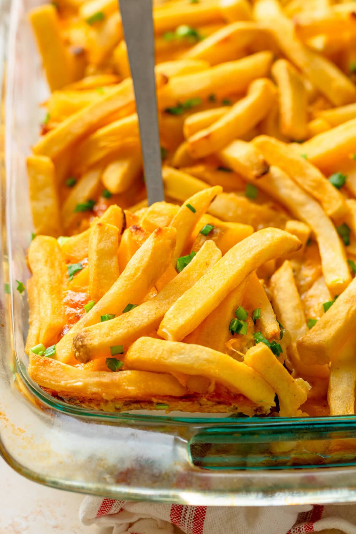 A spatula serving Cheeseburger French Fry Casserole from a glass baking pan.