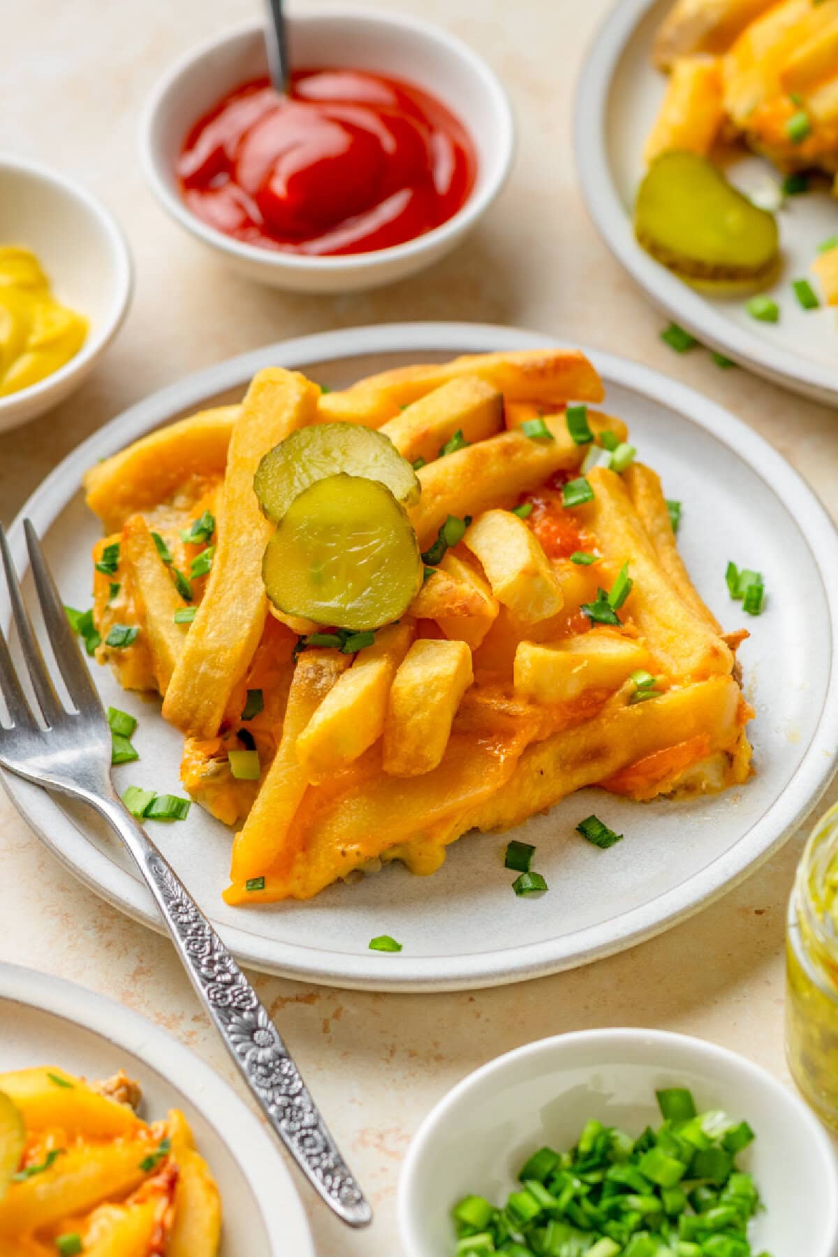 A serving of Cheeseburger French Fry Casserole on a white plate with toppings.