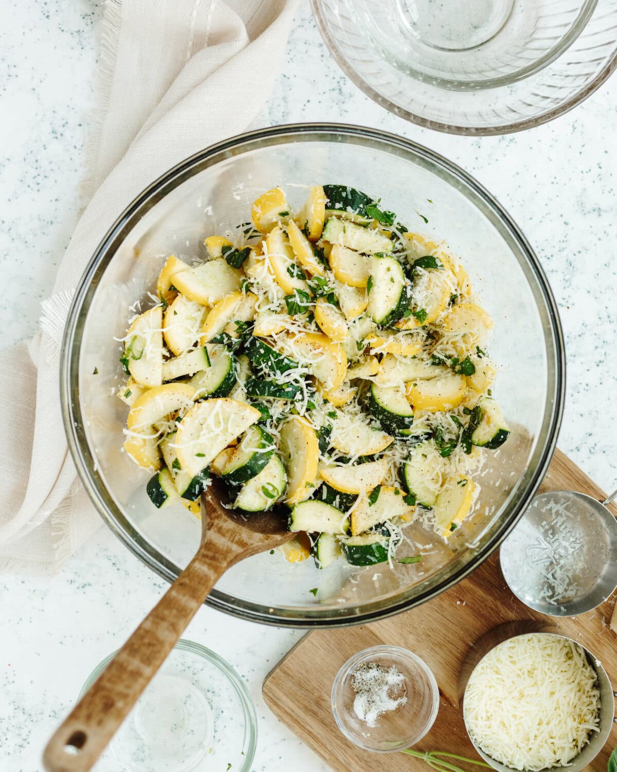 Squash and zucchini diced and mixed with fresh herbs, salt, pepper, and garlic in a mixing bowl.