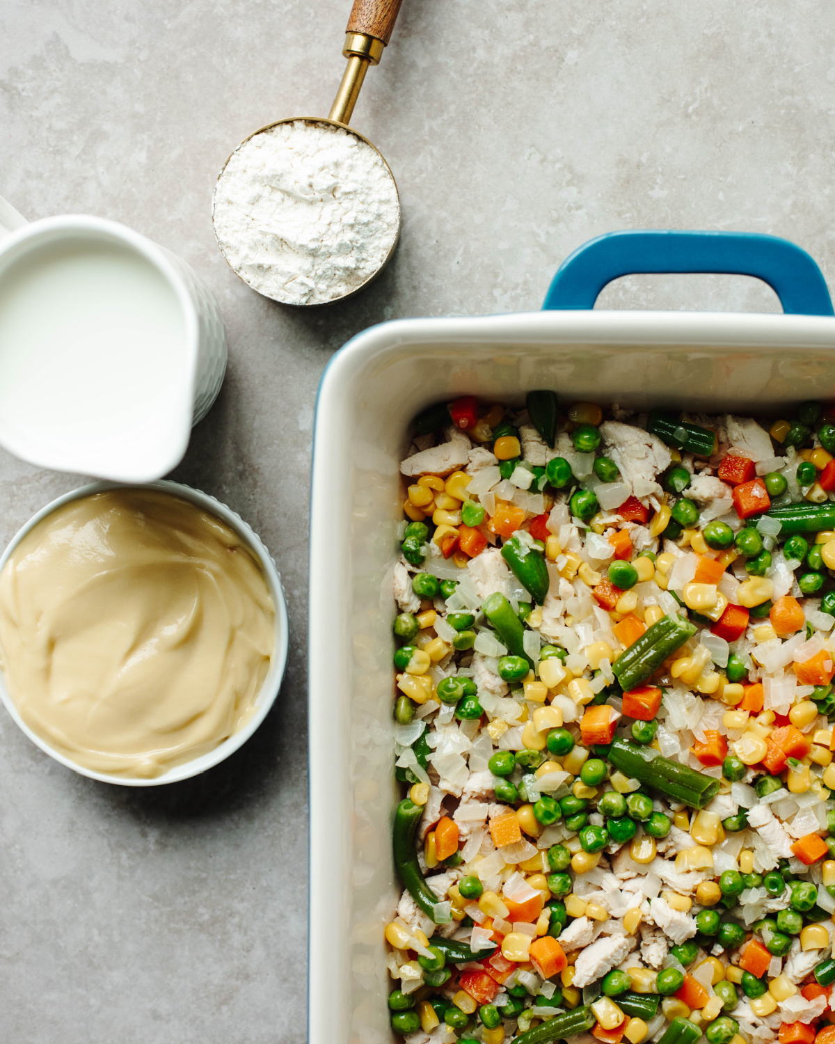 Mixed vegetables added with cooked chicken in a 9x13 baking pan.